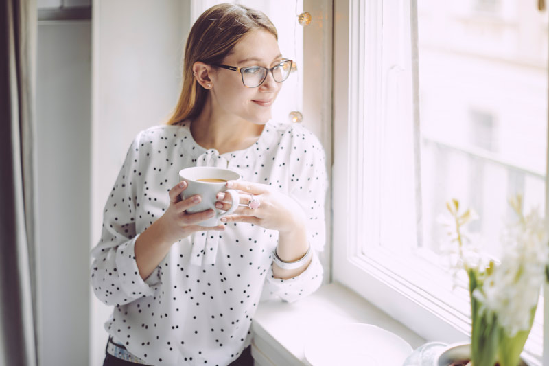 Woman standing by window enjoying the morning Woman standing by window