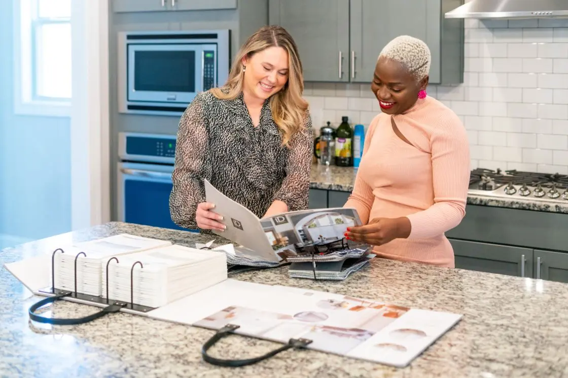 two women looking at budget blinds design book and smiling during a in-home consultation